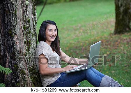 Teen girl sitting by tree using laptop View Large Photo Image Stock Photo - Teen girl sitting by tree using laptop. Fotosearch