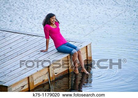 Teen girl sitting on dock with feet in water View Large Photo Image Stock Image - Teen girl sitting on dock with feet in water. Fotosearch