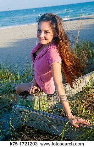 Stock Image - Teen girl sitting on fence in sand dune. Fotosearch