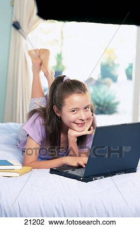 Stock Image - Teen girl using personal computer in bed. Fotosearch