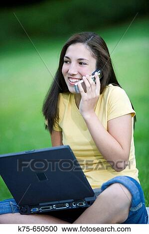 Stock Image - Teen using cell phone and laptop outdoors. Fotosearch