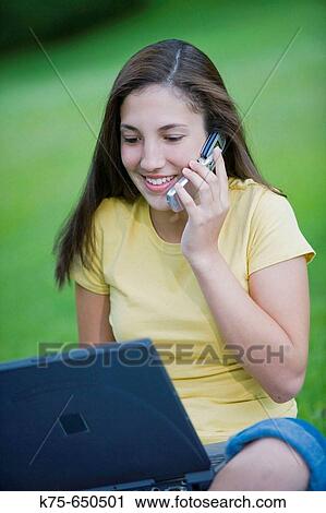 Stock Image - Teen using cell phone and laptop outdoors. Fotosearch
