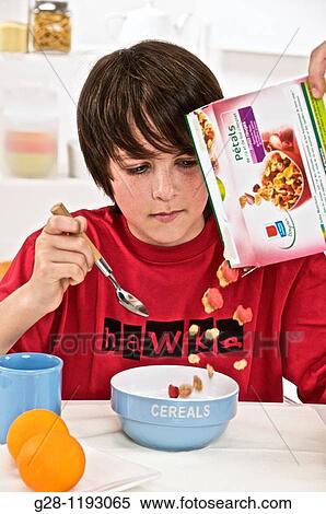 Stock Photography - teenage boy at breakfast time, in a red T shirt, pouring out cereals into a blue bowl, with blue mug and oranges. Fotosearch