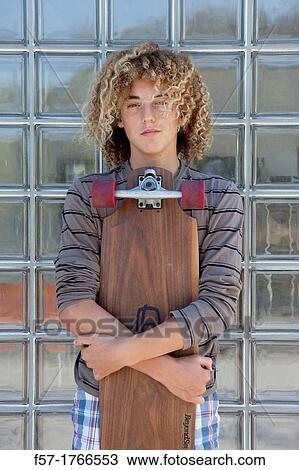 Stock Image - Teenage boy holding a long board. Fotosearch