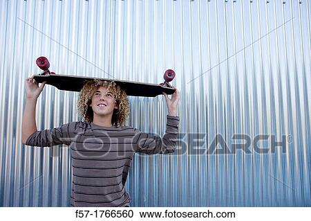 Teenage boy holding a longboard on his head View Large Photo Image Stock Image - Teenage boy holding a longboard on his head. Fotosearch