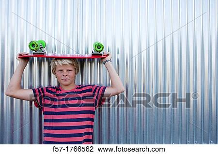 Stock Image - Teenage boy holding a longboard on his head. Fotosearch