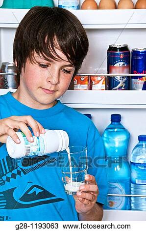 Stock Image - teenage boy in blue, in the kitchen, in front of the fridge, pouring himself a glass of milk. Fotosearch