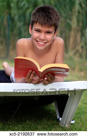 Teenage boy lying on a sun lounger and read a book outside in the garden View Large Photo Image Stock Photo - Teenage boy lying on a sun lounger and read a book outside in the garden. Fotosearch
