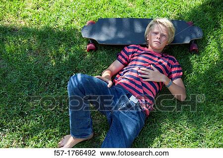 Stock Image - Teenage boy lying on the grass with his longboard. Fotosearch
