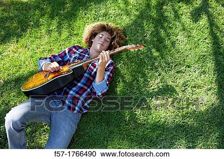 Teenage boy playing his guitar on the grass View Large Photo Image Stock Image - Teenage boy playing his guitar on the grass. Fotosearch