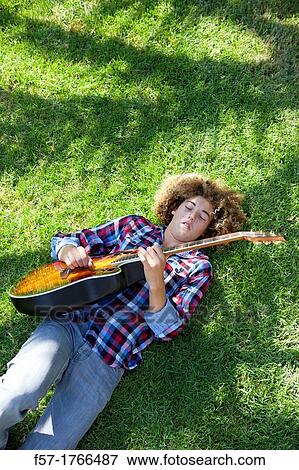 Teenage boy playing his guitar on the grass View Large Photo Image Stock Photo - Teenage boy playing his guitar on the grass. Fotosearch