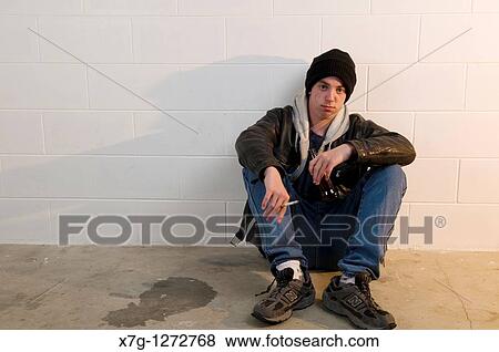 Stock Photo - Teenage boy sits with back against wall, drinking and smoking. Fotosearch