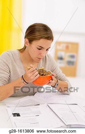 Stock Photograph - Teenage girl eating cereals for breakfast and doing her homework at the same time. Fotosearch