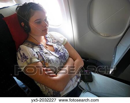 Teenage girl in headphones watching onboard TV in an airplane cabin. View Large Photo Image Stock Photo - Teenage girl in headphones watching onboard TV in an airplane cabin.. Fotosearch