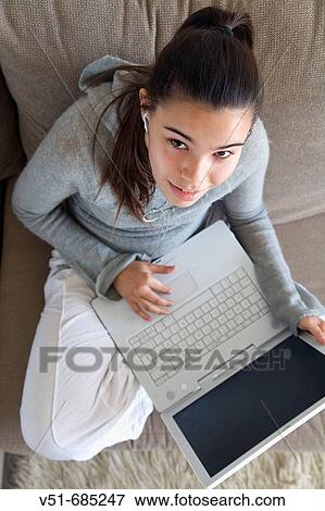 Teenage girl looking at camera and using laptop in the couch View Large Photo Image Stock Photo - Teenage girl looking at camera and using laptop in the couch. Fotosearch