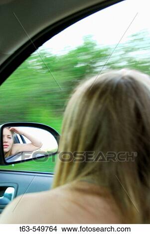 Picture - teenage girl looking at herself in side view mirror in the car. Fotosearch