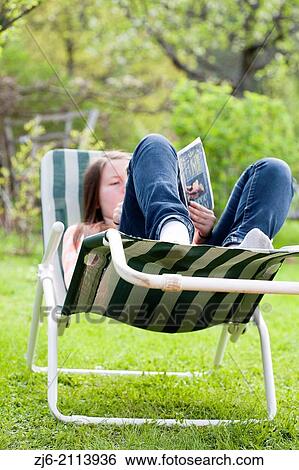 Teenage girl lying on a sun lounger and read a book outside in the garden. View Large Photo Image Stock Photograph - Teenage girl lying on a sun lounger and read a book outside in the garden.. Fotosearch