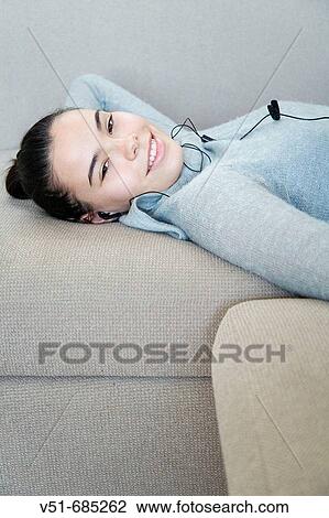 Stock Image - Teenage girl lying on the couch listening to music. Fotosearch