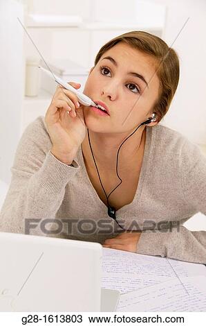 Stock Image - Teenage Girl thinking and doing her homework at home with a computer. Fotosearch