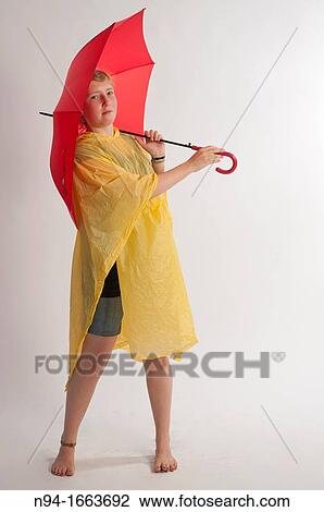 Stock Image - Teenage girl with yellow rain gear protected with red umbrella.. Fotosearch