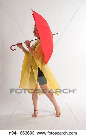 Stock Image - Teenage girl with yellow rain gear protected with red umbrella.. Fotosearch