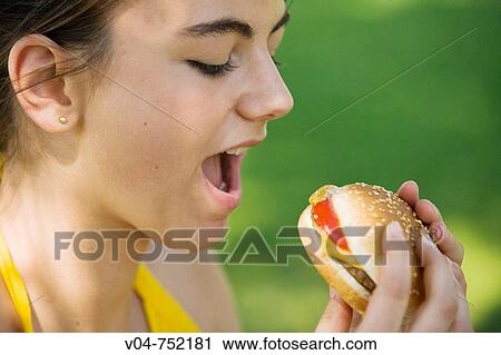 Teenaged girl biting into a hamburger outdoors View Large Photo Image Stock Image - Teenaged girl biting into a hamburger outdoors. Fotosearch