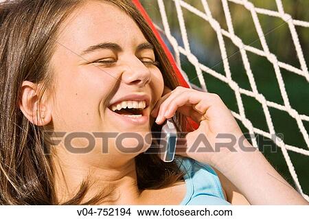 Teenaged girl bursting into laughter at her cell phone in a hammock outdoors View Large Photo Image Picture - Teenaged girl bursting into laughter at her cell phone in a hammock outdoors. Fotosearch