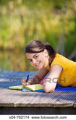 Teenaged girl lying on a footbridge and writing in her diary, smiling at the camera View Large Photo Image Picture - Teenaged girl lying on a footbridge and writing in her diary, smiling at the camera. Fotosearch
