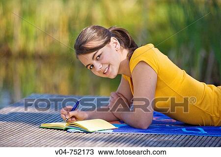 Teenaged girl lying on a footbridge and writing in her diary, smiling at the camera View Large Photo Image Stock Image - Teenaged girl lying on a footbridge and writing in her diary, smiling at the camera. Fotosearch