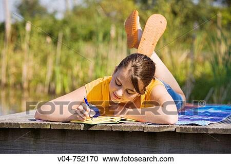 Stock Image - Teenaged girl lying on footbridge and writing in her diary with a slow smile. Fotosearch