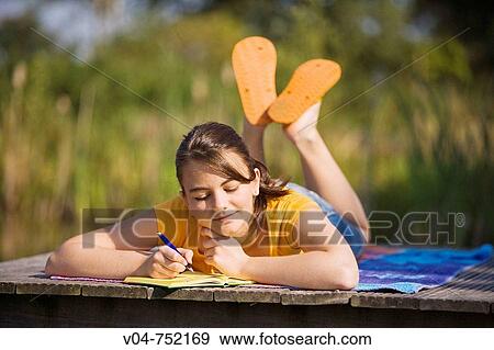 Stock Photo - Teenaged girl lying on plank and writing in her diary smiling. Fotosearch