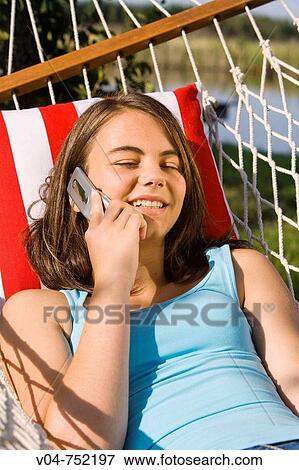 Teenaged girl talking and smiling on her cell phone in a hammock outdoors View Large Photo Image Stock Photo - Teenaged girl talking and smiling on her cell phone in a hammock outdoors. Fotosearch