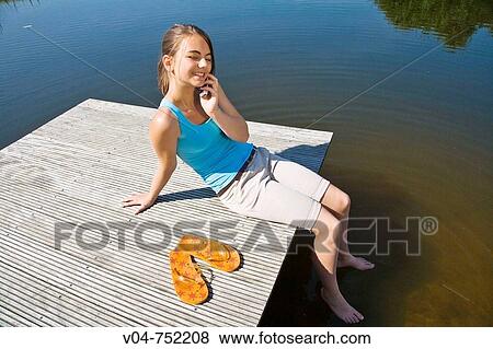 Teenaged girl talking on her cell phone outdoors at a lake View Large Photo Image Stock Photo - Teenaged girl talking on her cell phone outdoors at a lake. Fotosearch