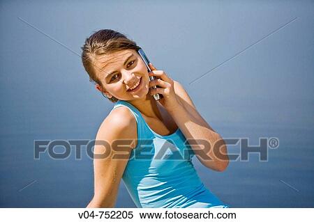 Teenaged girl using her cell phone and smiling at the camera outdoors at a lake View Large Photo Image Stock Photography - Teenaged girl using her cell phone and smiling at the camera outdoors at a lake. Fotosearch