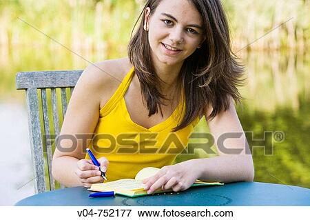 Teenaged girl writing in her diary and smiling at the camera outdoors View Large Photo Image Stock Photo - Teenaged girl writing in her diary and smiling at the camera outdoors. Fotosearch