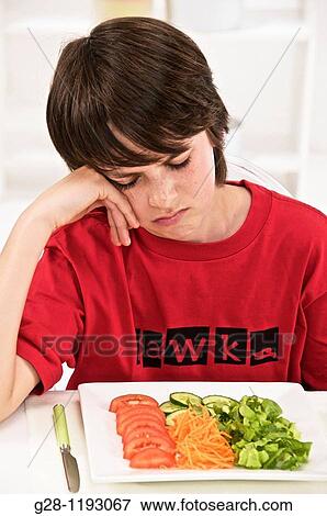 Stock Photo - teenager boy not wanting to eat a plate of salad, natural vegetables,. Fotosearch