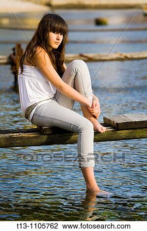 Stock Image - Teenager girl is sitting on an old rotten pier. Fotosearch
