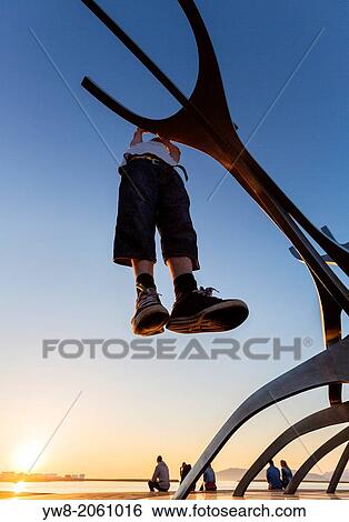 Stock Photograph - Teenager hanging on metal sculpture known as The Solfar, Reykjavik, Iceland.. Fotosearch