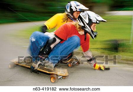Stock Image - Teenagers riding longboards downhill.. Fotosearch
