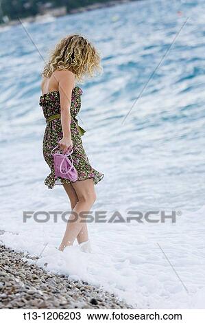 Stock Image - Testing water young woman in a flowery dress. Fotosearch
