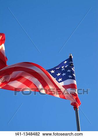 Stock Image - The American Flag blowing in the wind against a blue sky. Fotosearch