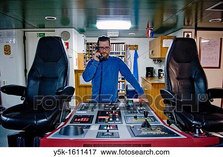 Stock Photo - The captain of the container-vessel MV Flintercape uses the marine-phone or ships communication device to communicate with the shore, where he can order a pilot to enter the harbor.. Fotosearch