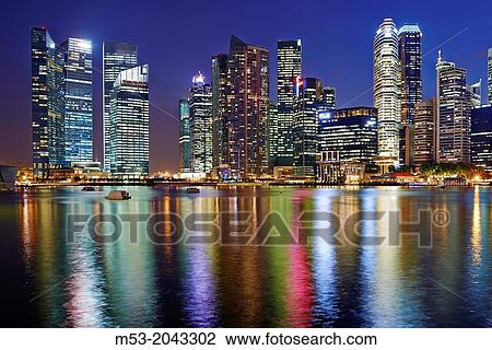 Stock Image - The Central Business District by night. In the foreground the water of Marina bay. Singapore.. Fotosearch