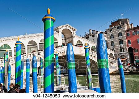 Stock Image - The famous Rialto Bridge with colorful poles in the foreground in Venice, Italy, Europe. Fotosearch