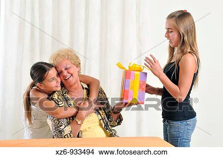 The girl passes the present to the grandma Sister hugging grandma View Large Photo Image Picture - The girl passes the present to the grandma Sister hugging grandma. Fotosearch