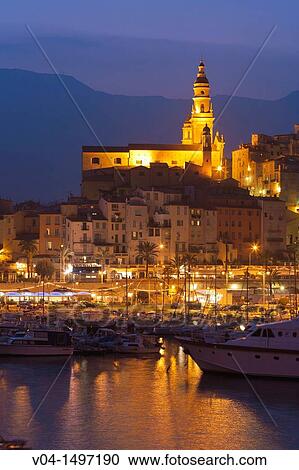 Stock Image - The illuminated Basilique St-Michel-Archange and harbor at dusk, Menton, France, Europe. Fotosearch