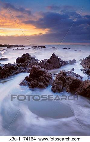 The incoming tide washing over the rocks at dusk at Westward Ho! in Devon, England View Large Photo Image Picture - The incoming tide washing over the rocks at dusk at Westward Ho! in Devon, England. Fotosearch