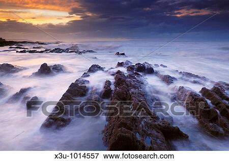 The incoming tide washing over the rocks at dusk at Westward Ho! in Devon, England View Large Photo Image Stock Photo - The incoming tide washing over the rocks at dusk at Westward Ho! in Devon, England. Fotosearch