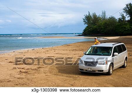 Stock Photo - The pristine beach area of Hanalei Bay may be the most famous location on Kauai. The ideal scenic location has been cast in numerous movies and images. It is easily recognizable by the Hanalei Bay pier. A girl checks out the surf in the distance.. Fotosearch