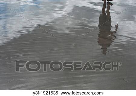 Stock Photography - The reflection of a man walking on the exposed mudflats at low tide.. Fotosearch